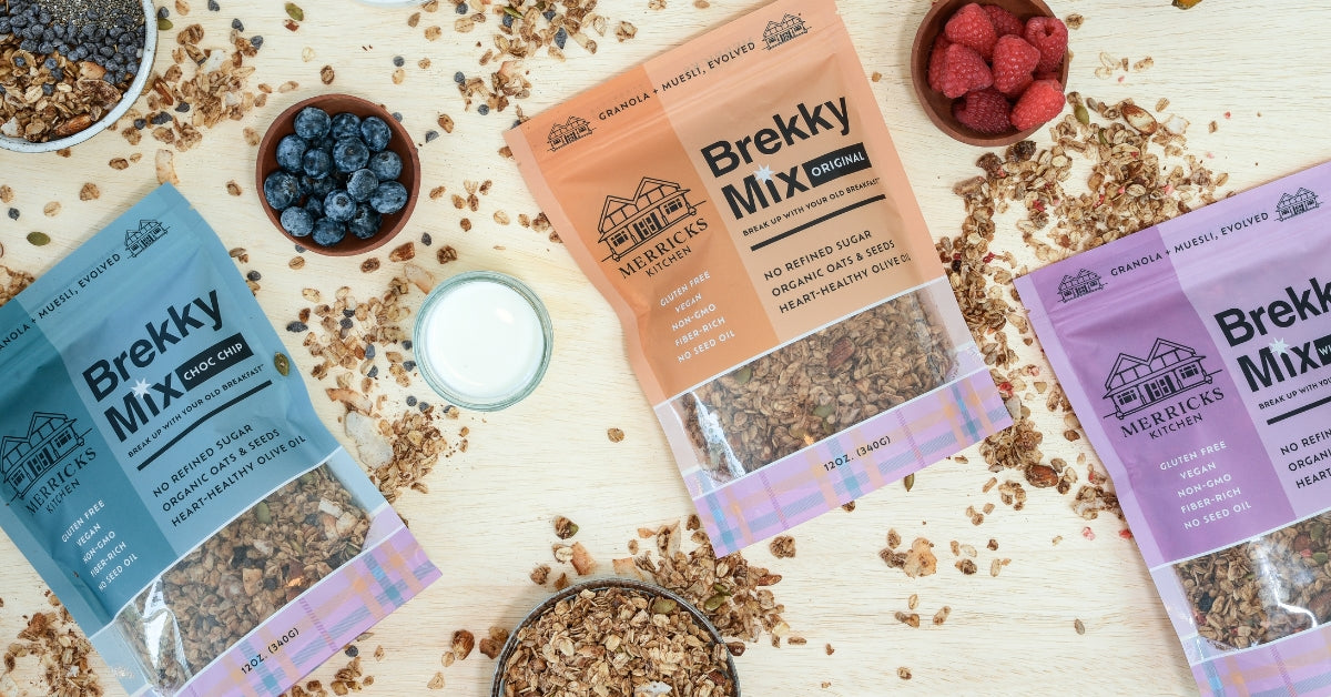 Brekky Mix packages on a wooden surface with healthy granola ingredients like oats, nuts and seeds.