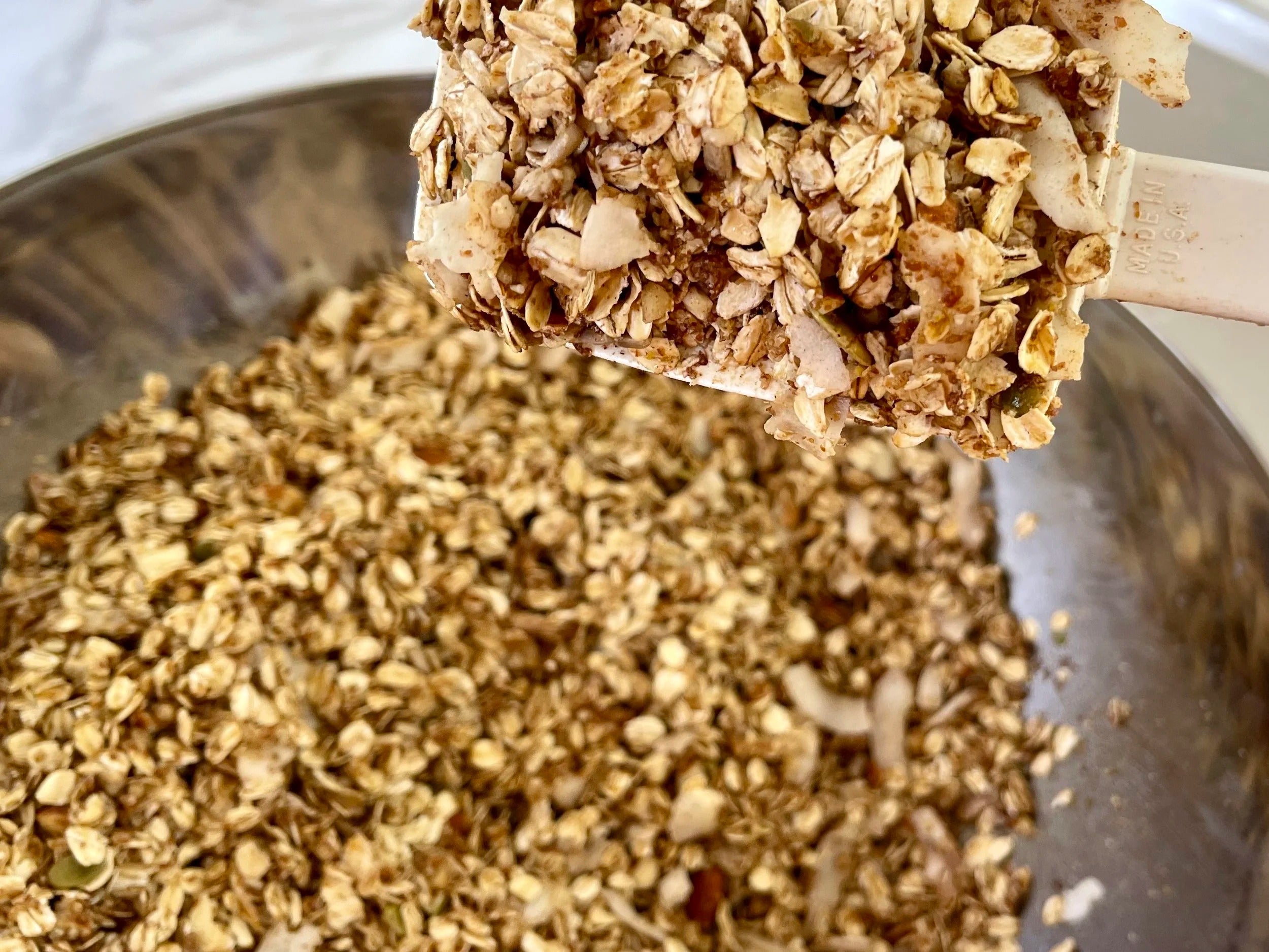 Close-up of healthy granola on a wooden spoon with a metal bowl in the background