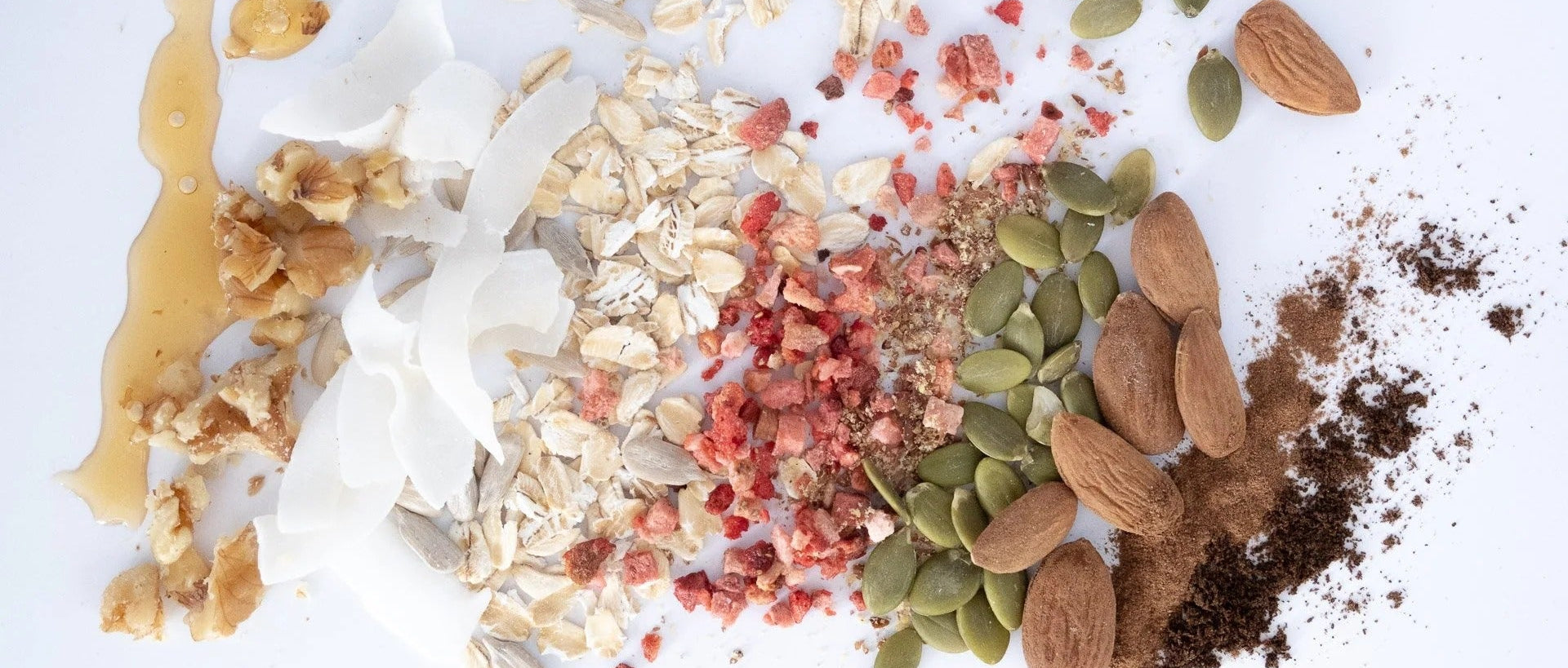 Assorted healthy granola ingredients including nuts, seeds, and dried fruits on a white background