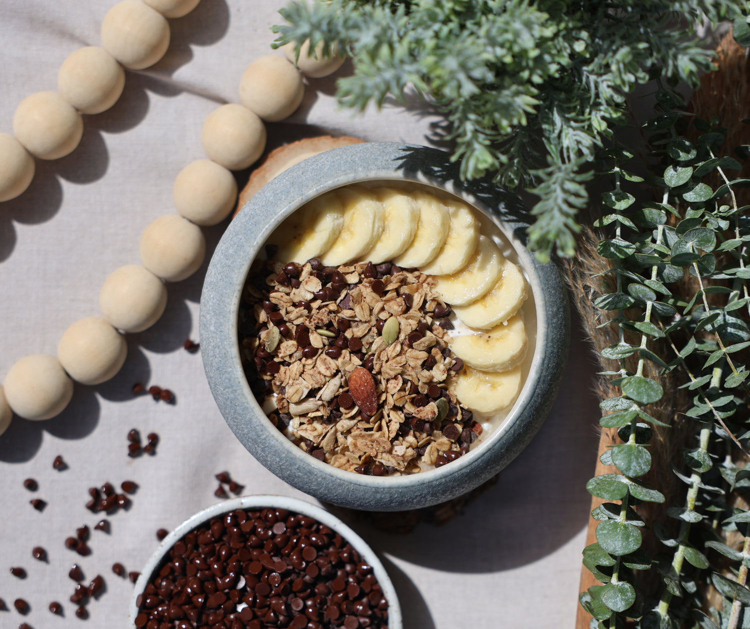 Bowl of healthy choc chip granola with bananas on a light surface with decorative elements