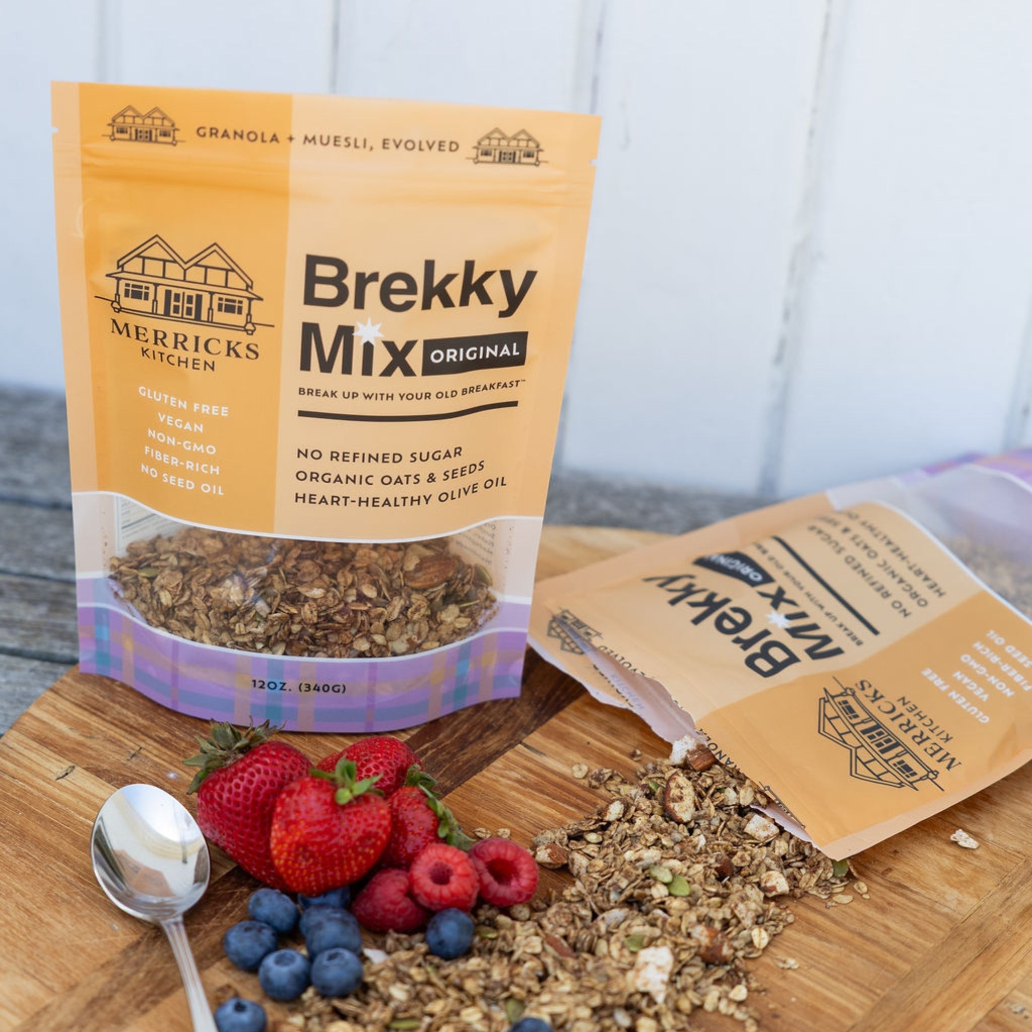 Merricks Kitchen Brekky Mix Original healthy granola packages on a wooden surface with berries and granola.