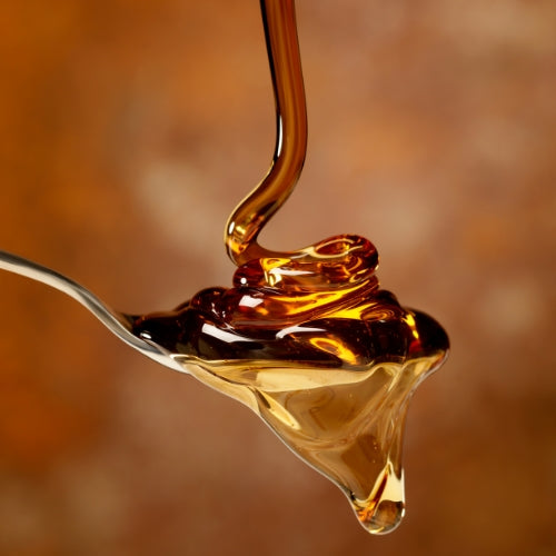 Maple syrup being dripped from a spoon onto another spoon against a blurred background