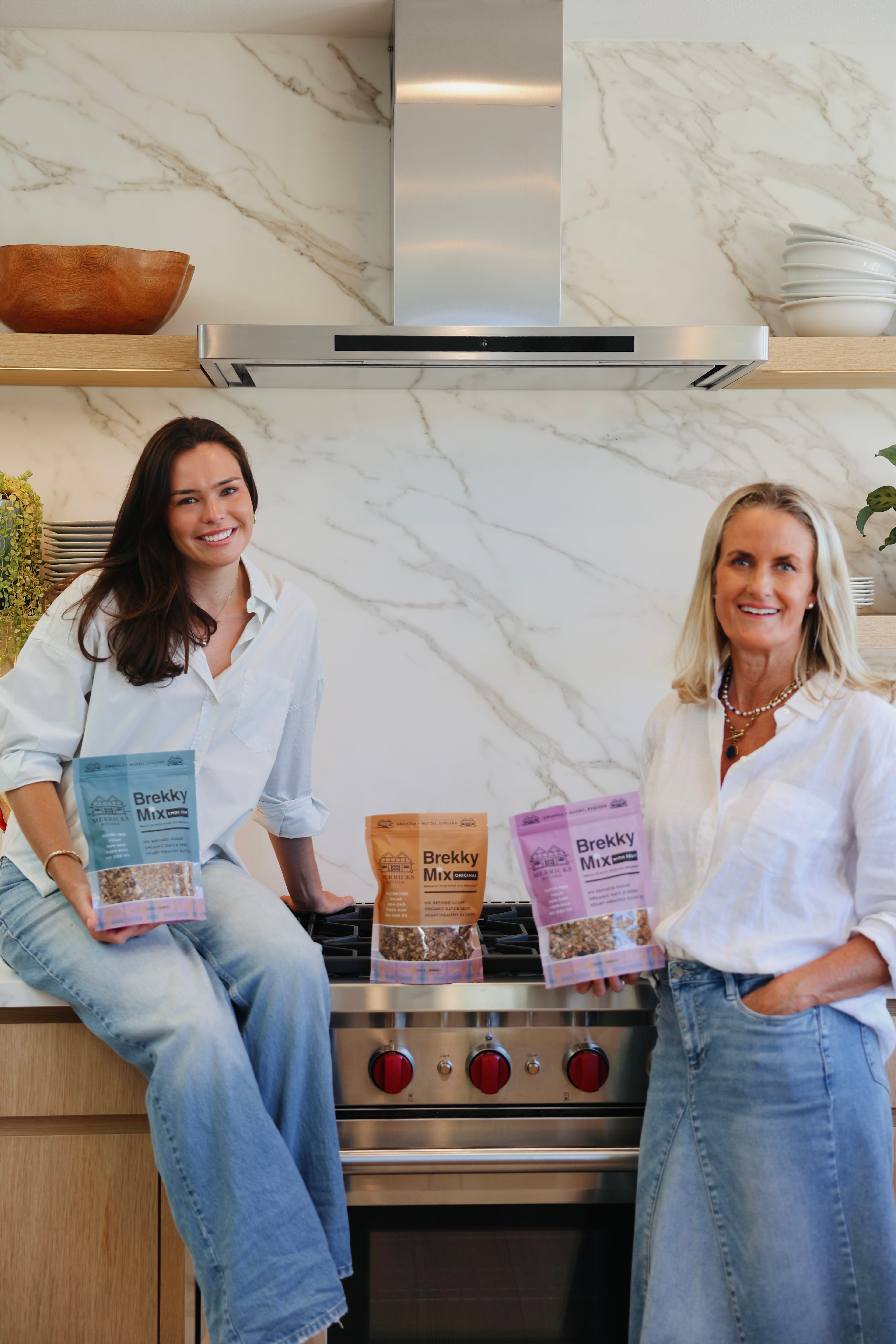 A mother and grown up daughter in a kitchen holding healthy granola food products.
